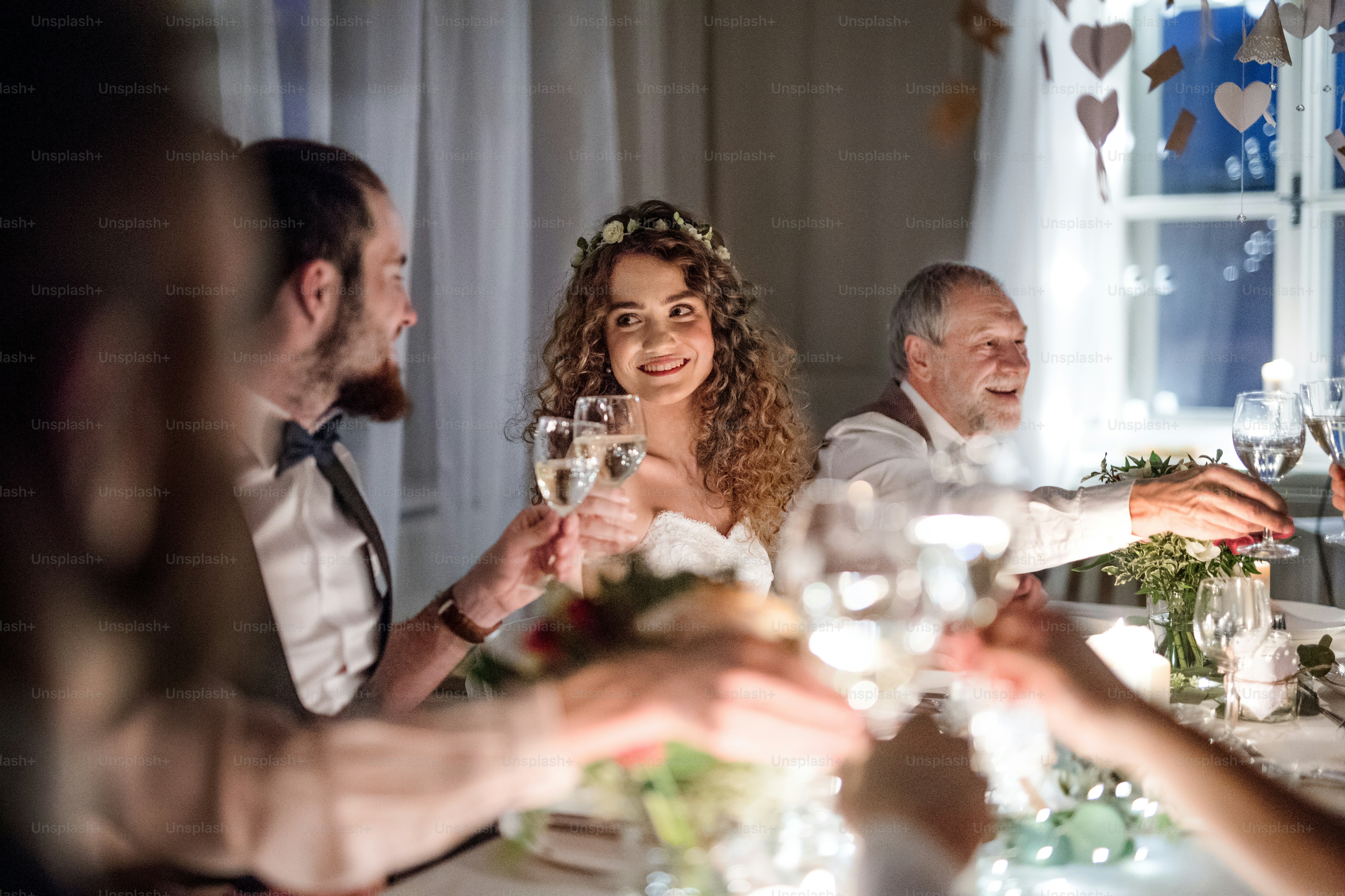 A bride and groom and other guests sitting at a table on a wedding, clinking glasses.
