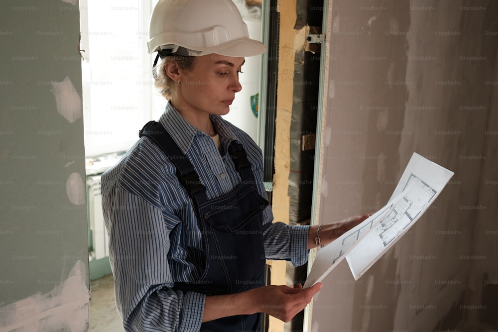 a woman in a hard hat and overalls holding a piece of paper