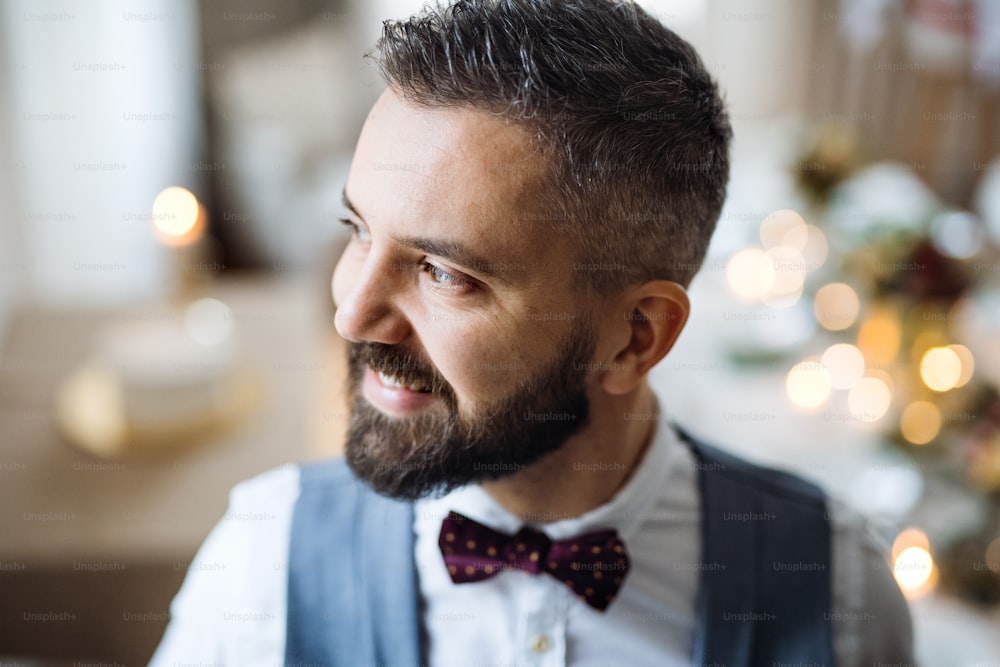 A portrait of a hipster mature man standing indoors in a room set for a party, looking away. A close-up.