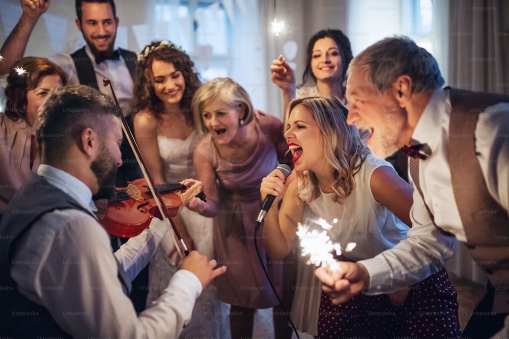 Uma jovem noiva alegre, noivo e outros convidados dançando, cantando e tocando violino em uma recepção de casamento.