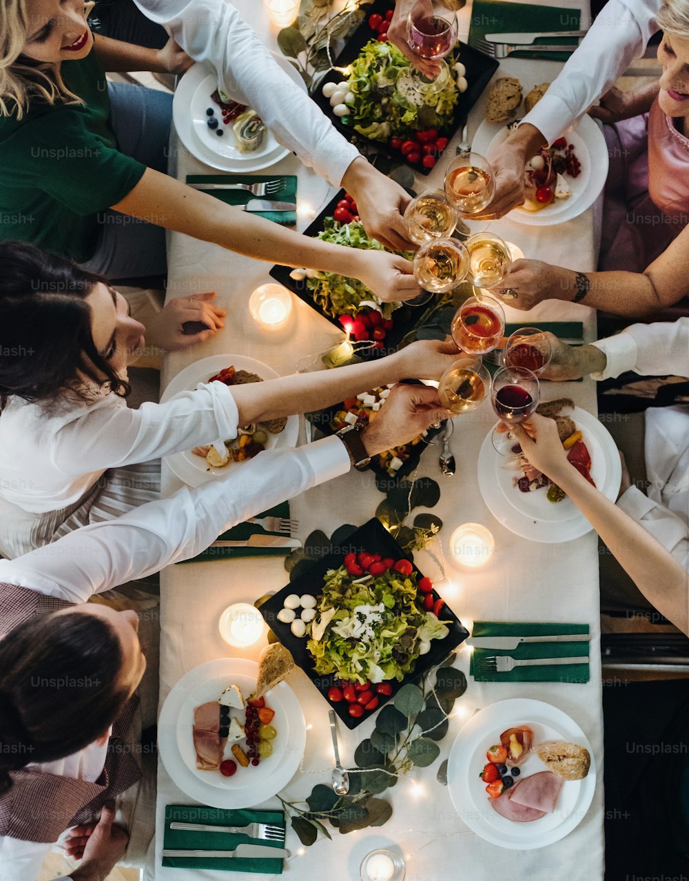 Una sección media de grandes familiares o amigos sentados en una mesa en una fiesta de cumpleaños en el interior, tintineando vasos. Una vista superior.