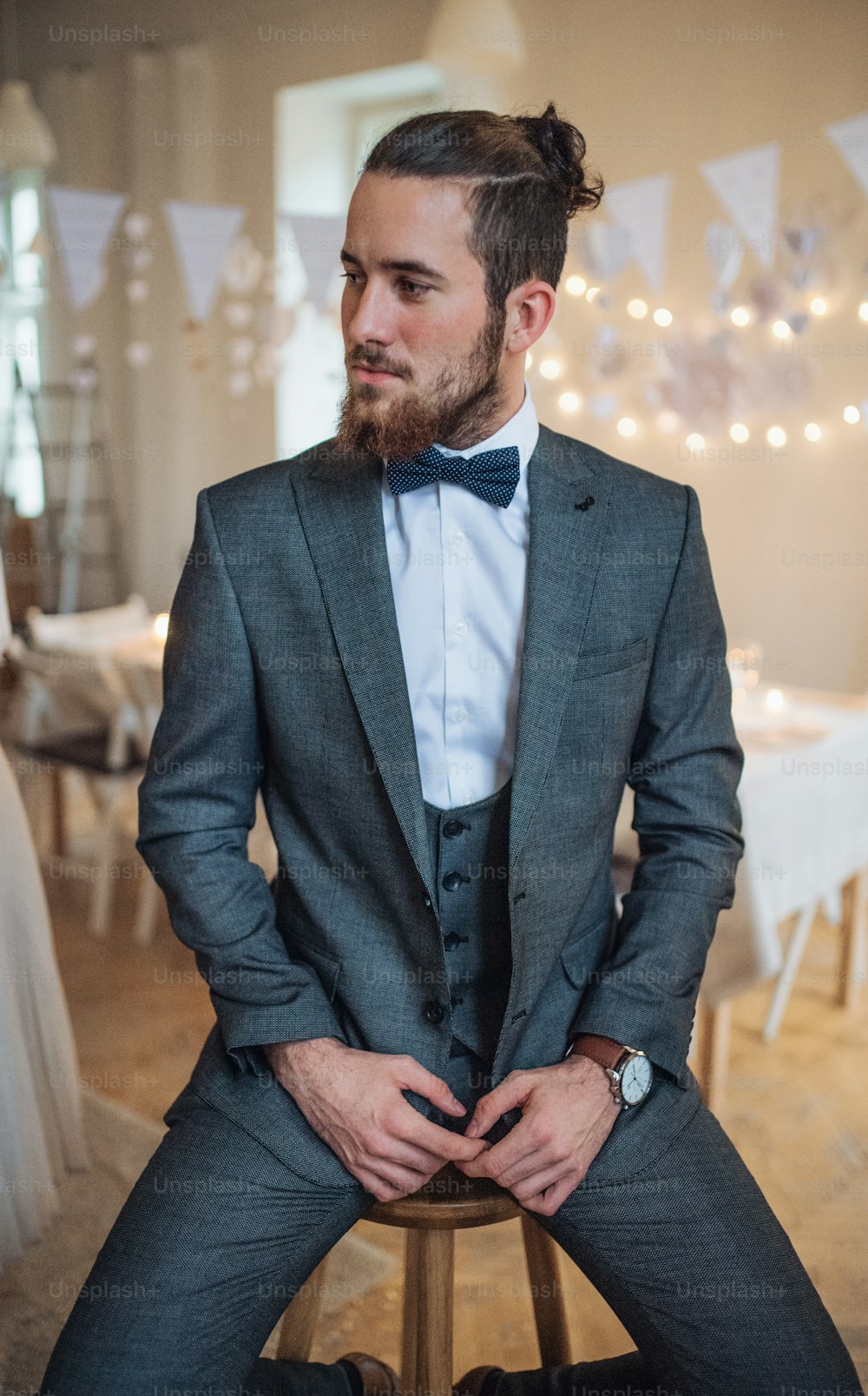 Un beau jeune homme hipster en costume formel assis sur un tabouret lors d’une fête à l’intérieur, détournant le regard.