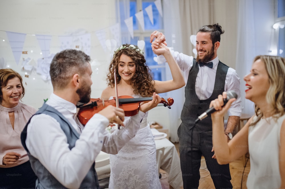 A young cheerful bride, groom and other guests dancing, singing and playing violin on a wedding reception.