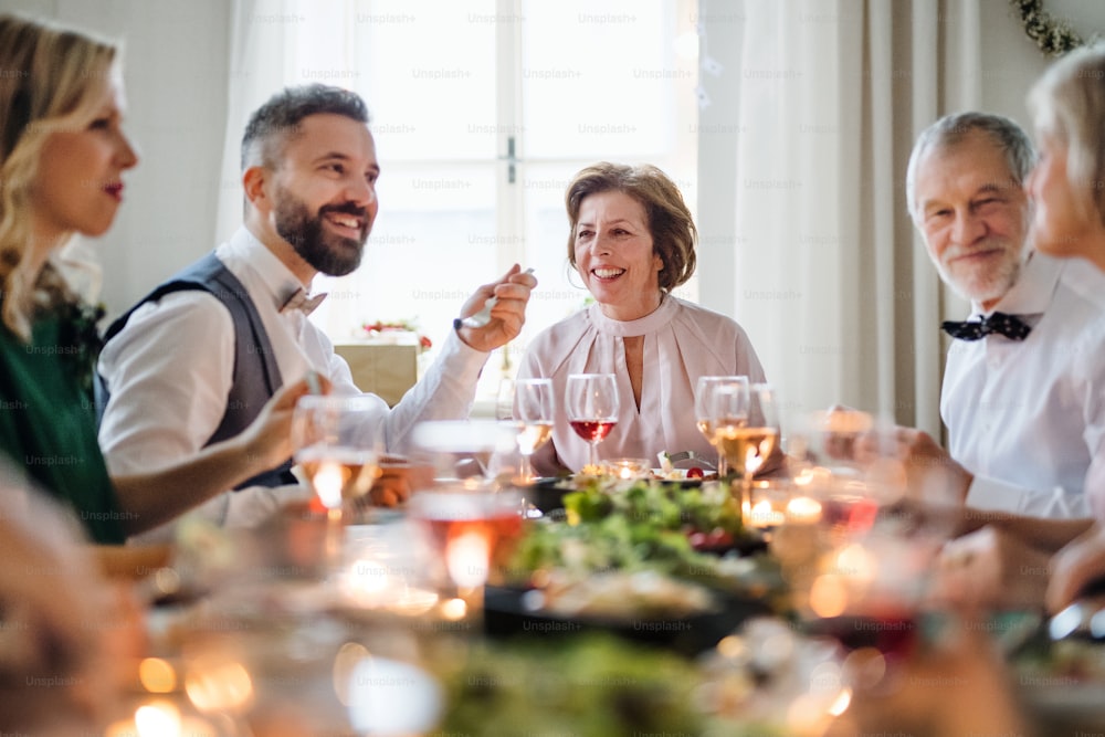 Una gran familia feliz sentada en una mesa en una fiesta de cumpleaños interior, comiendo.