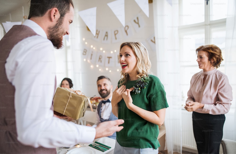 家族の誕生日や記念日のパーティーで驚いた若い女性に贈り物をする男性。