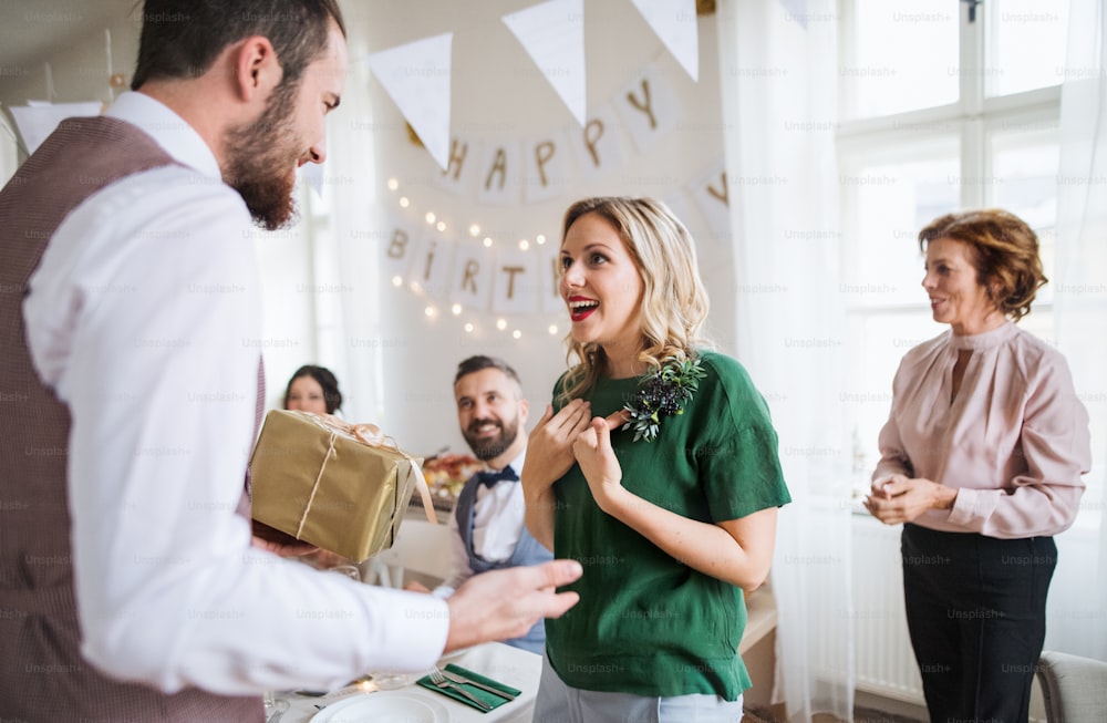 Un homme offrant un cadeau à une jeune femme surprise lors d’un anniversaire de famille ou d’une fête d’anniversaire.