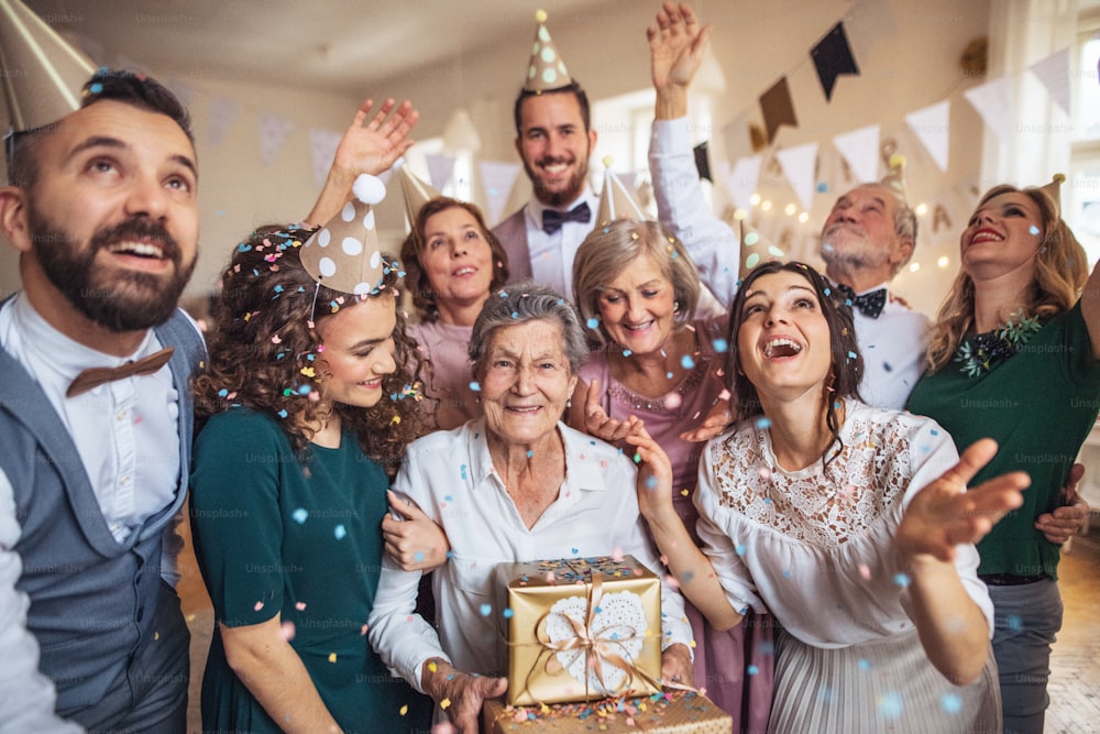 Ein Porträt einer Mehrgenerationenfamilie mit Geschenken, die auf einer Geburtstagsfeier drinnen stehen.