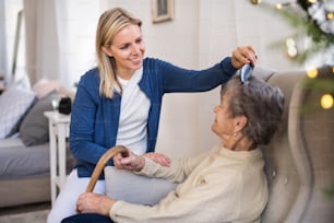 A health visitor combing hair of senior woman sitting on a sofa at home at Christmas time.