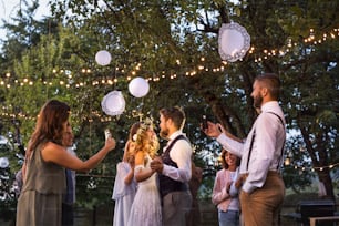 Convidados com smartphones tirando foto de uma noiva e noivo dançando na recepção do casamento do lado de fora. Uma noite no quintal.