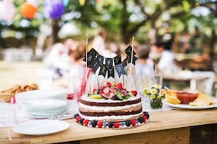 Family celebration outside in the backyard. Big garden party. Birthday party. Close up of a fruit birthday cake.