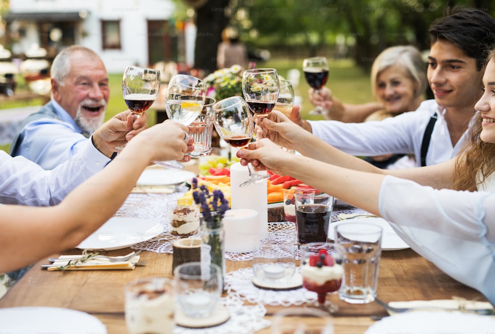 Festa no jardim ou celebração familiar do lado de fora no quintal. Pessoas sentadas ao redor da mesa, piscando os óculos.