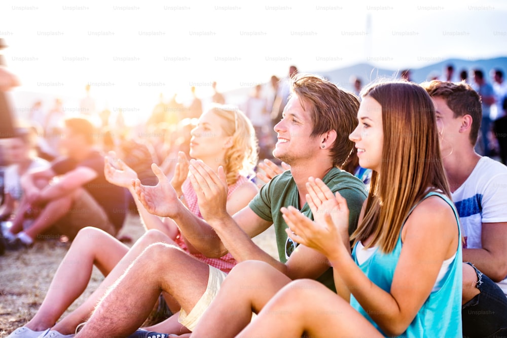 Group of teenagers at summer music festival, sitting on the ground , hipster boy in green t-shirt