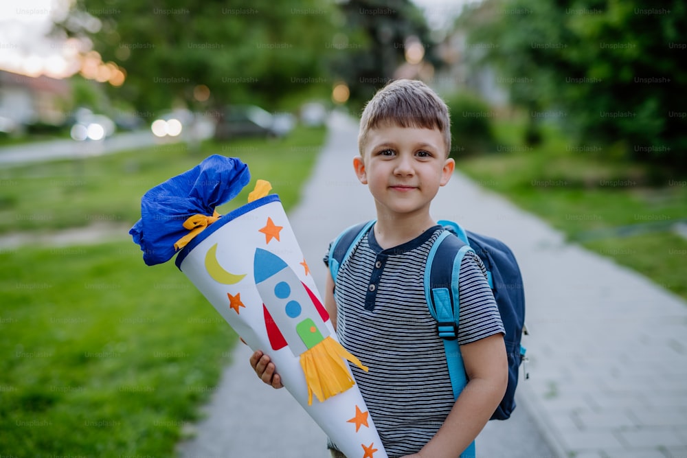 A little kid boy with school satchel on first day of school, holding school cone with gifts
