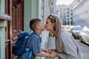 Mutter küsst ihren kleinen Sohn auf dem Weg zur Schule, und eine Mutter und ein Junge verabschieden sich vor der Schule.
