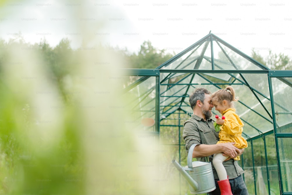 A gather with his little daughter bonding in front of eco greenhouse, sustainable lifestyle.