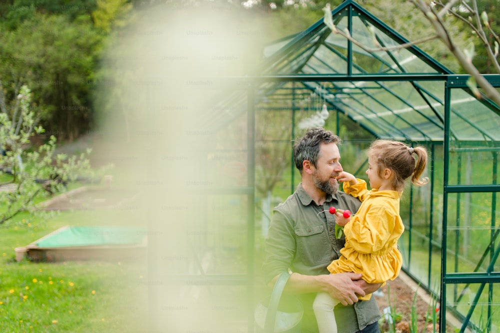 Una reunión con su pequeña hija uniéndose frente a un invernadero ecológico, estilo de vida sostenible.