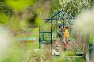 A gather with his little daughter bonding in front of eco greenhouse, sustainable lifestyle.