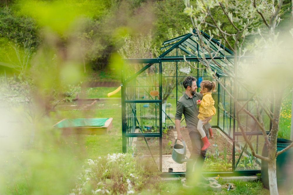 A gather with his little daughter bonding in front of eco greenhouse, sustainable lifestyle.