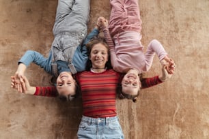 A top view of happy three sisters kids lying on floor and looking at camera.