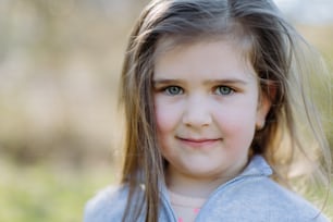 Porträt eines hübschen Kindermädchens, das im Sommerpark steht und glücklich lächelnd in die Kamera schaut.