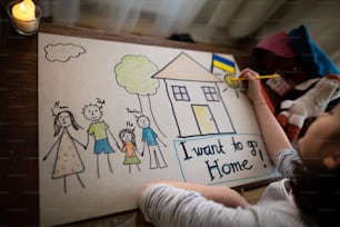 A top view of Ukrainian refugee schoolgirl missing home and drawing her family. Ukrainian war concept.