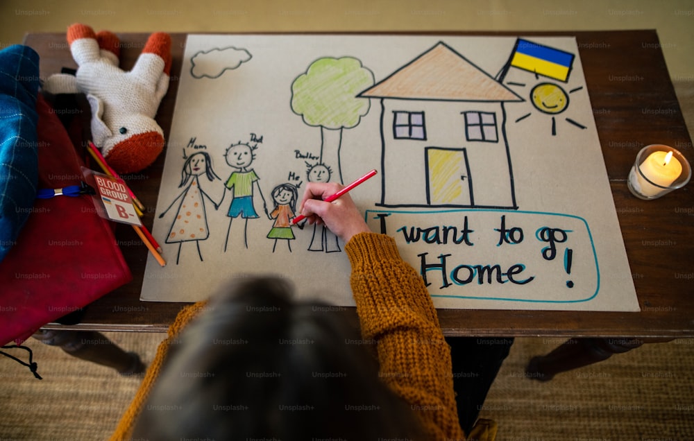 Una vista dall'alto della studentessa rifugiata ucraina che manca a casa e disegna la sua famiglia. Concetto di guerra ucraina.