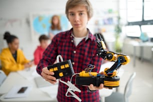 Estudante universitário segurando seu brinquedo robótico construído em uma sala de aula de robótica científica na escola.