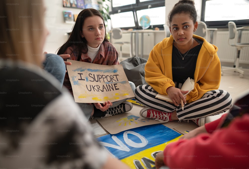 Teenager sitzen im Kreis in einem Klassenzimmer mit Plakaten zur Unterstützung der Ukraine, kein Kriegskonzept.