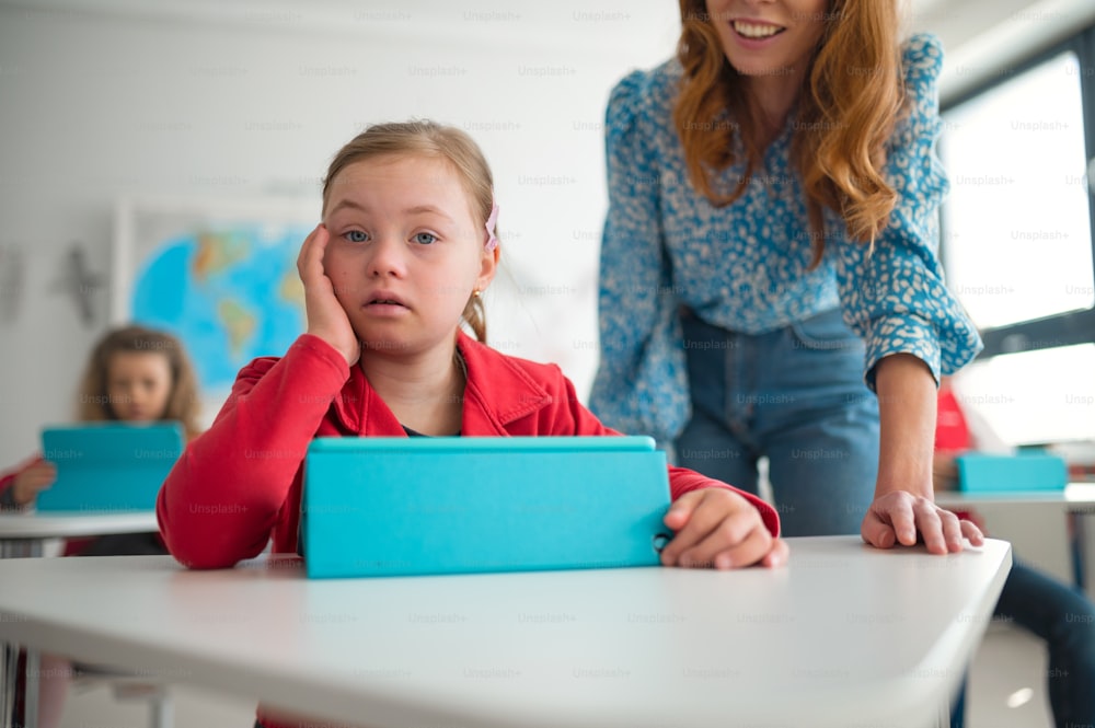 Ein Down-Syndrom-Schülermädchen, das Tablet mit Hilfe des Lehrers während des Unterrichts in der Schule verwendet, Integrationskonzept.