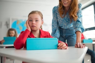 Una colegiala con síndrome de Down usando tableta con la ayuda del maestro durante la clase en la escuela, concepto de integración.