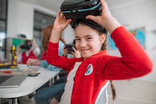 A happy schoolgirl wearing virtual reality goggles at school in computer science class