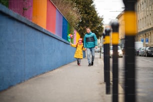 Ein Vater, der seine kleine Tochter mit Down-Syndrom zur Schule bringt, draußen auf der Straße.