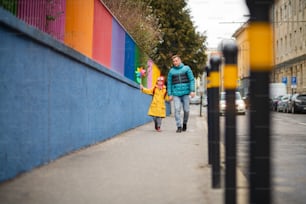 Um pai levando sua filhinha com síndrome de Down para a escola, ao ar livre na rua.