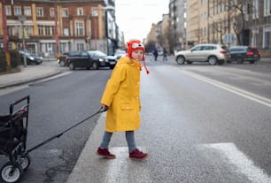 Una bambina con sindrome di Down che attraversa la strada e tira il carrello.