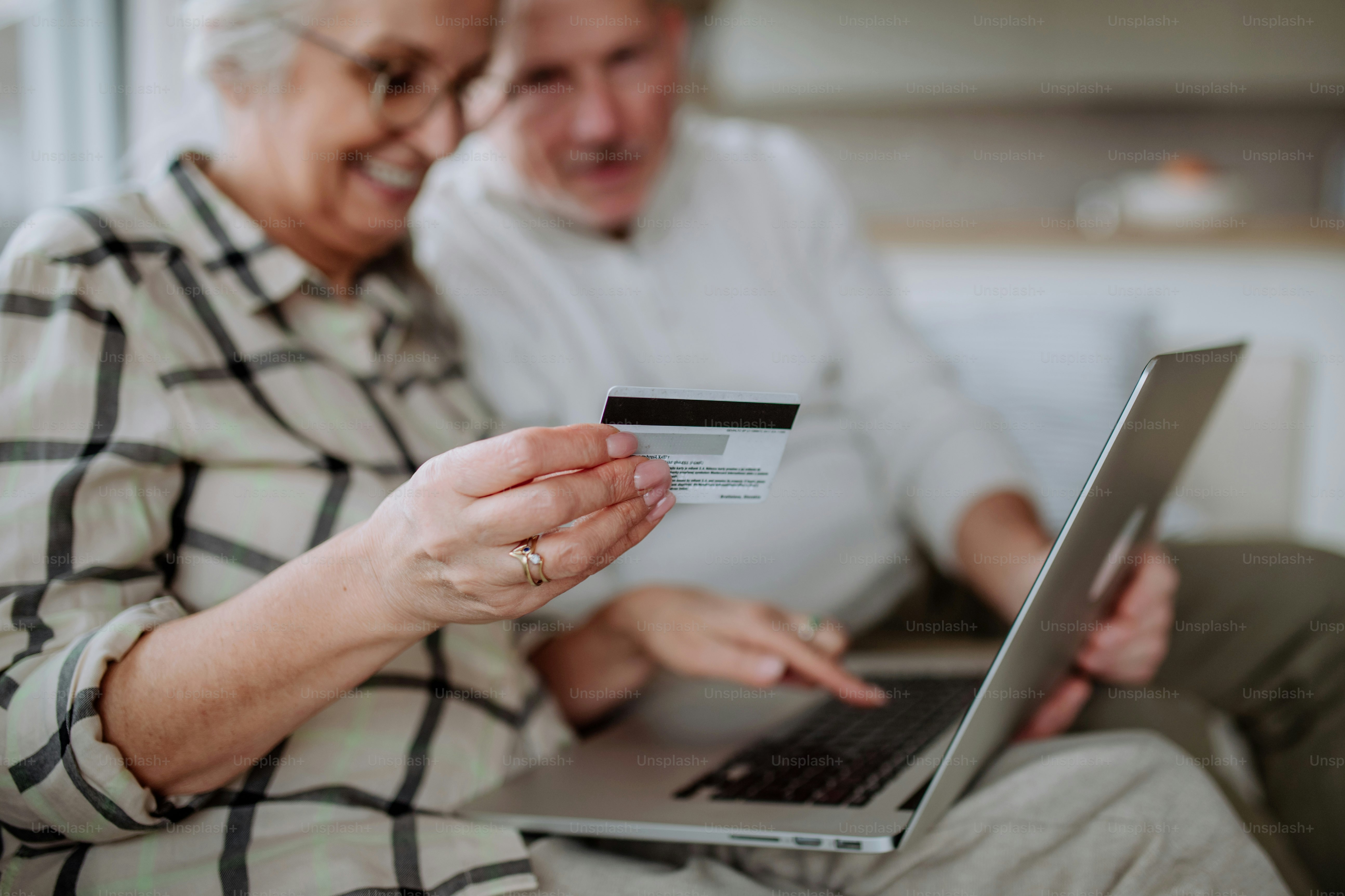 Pasangan senior duduk di sofa dan berbelanja online dengan laptop dan kartu kredit