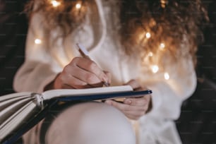 A happy young woman sitting on sofa and writing in diary in the evening in cozy hyyge living room, close-up