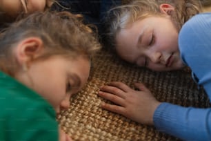 A top view of of tired little girls friends lying on back on floor and sleeping.