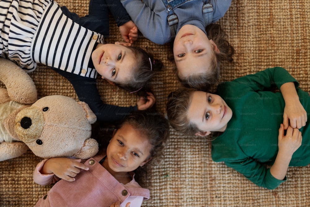 A top view of of little girls friends lying on back on floor and looking at camera.