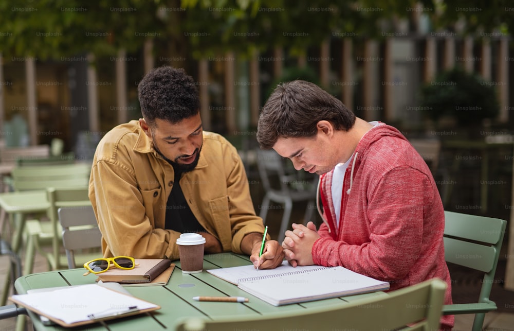 ダウン症の青年で、メンタリングの友人が屋外のカフェに座って勉強している。
