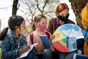 Uma professora com crianças pequenas sentadas ao ar livre no parque da cidade, aprendendo educação em grupo e conceito de coronavírus.