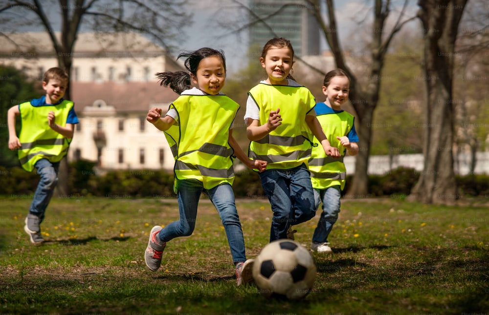 Niños pequeños felices jugando al fútbol al aire libre en el parque de la ciudad, aprendiendo el concepto de educación grupal.