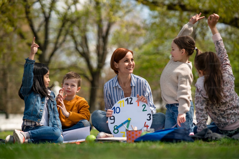 Un insegnante con bambini piccoli seduti all'aperto nel parco cittadino, imparando il concetto di educazione di gruppo.