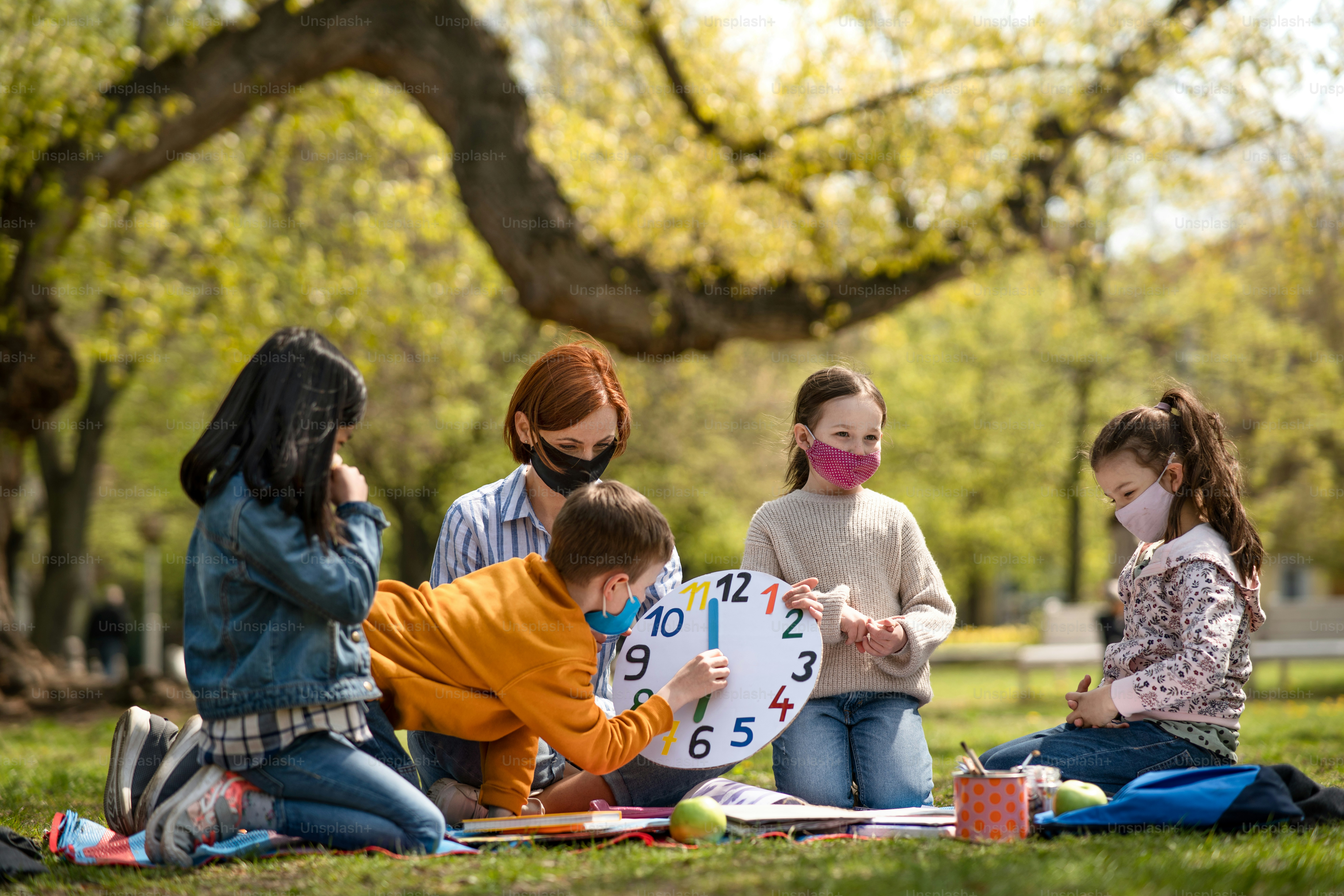 A teacher with small children sitting outdoors in city park, learning ...