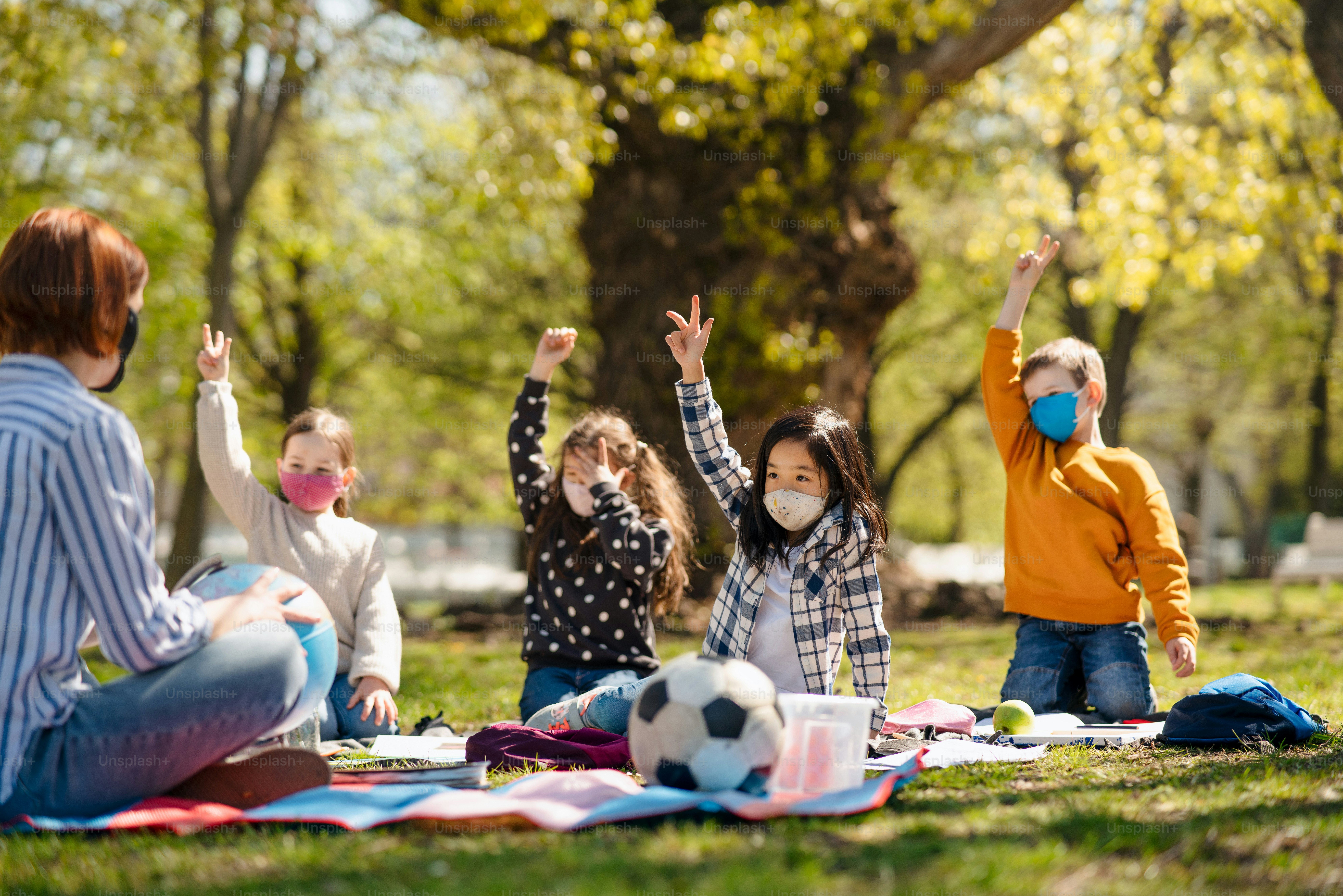 Ein Lehrer mit kleinen Kindern, die im Freien im Stadtpark sitzen, Lerngruppenunterricht und Coronavirus-Konzept.