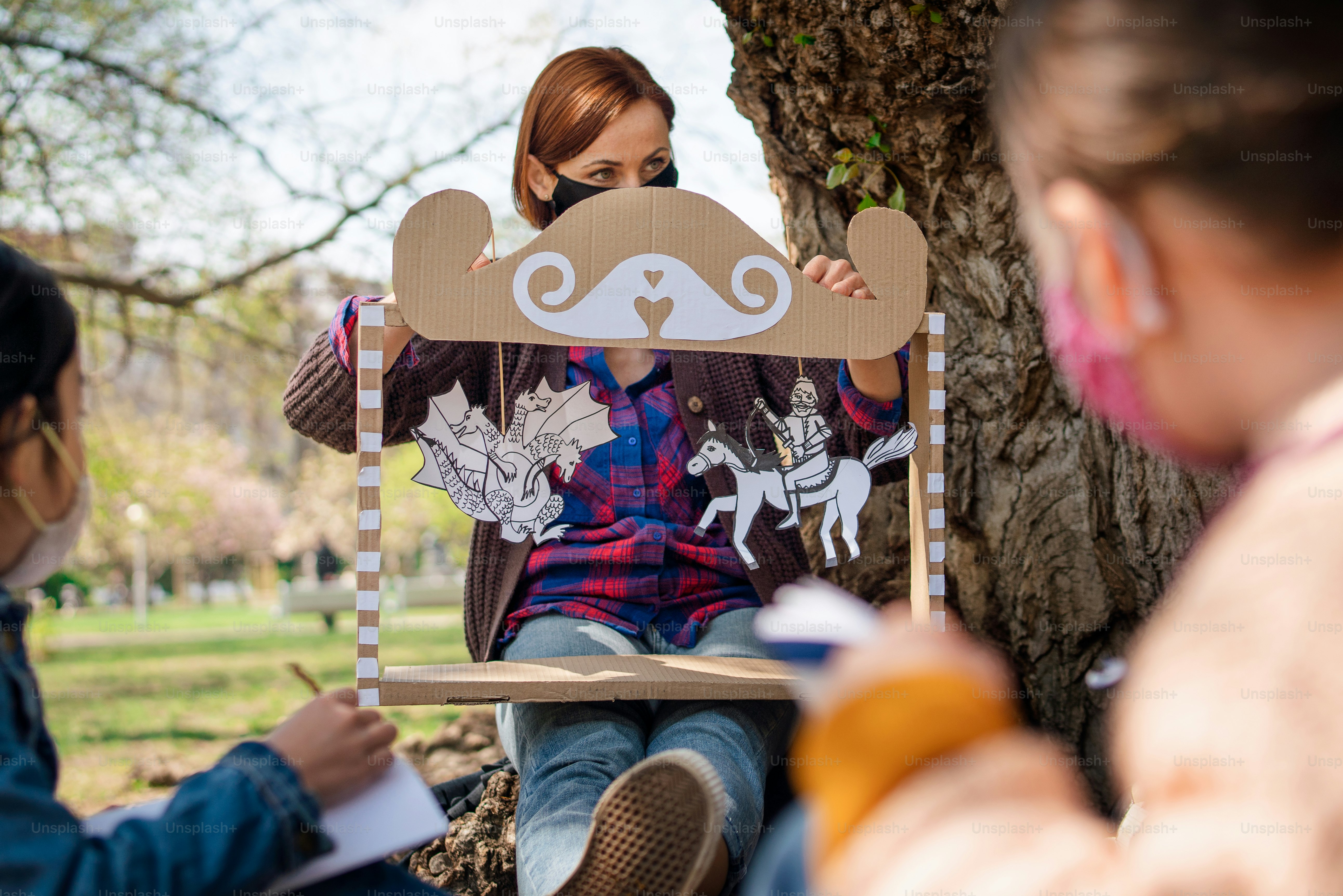 A teacher with small children sitting outdoors in city park, learning group education and coronavirus concept.
