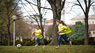 都市公園で屋外でサッカーをする幸せな小さな女の子、グループ教育のコンセプトを学ぶ。