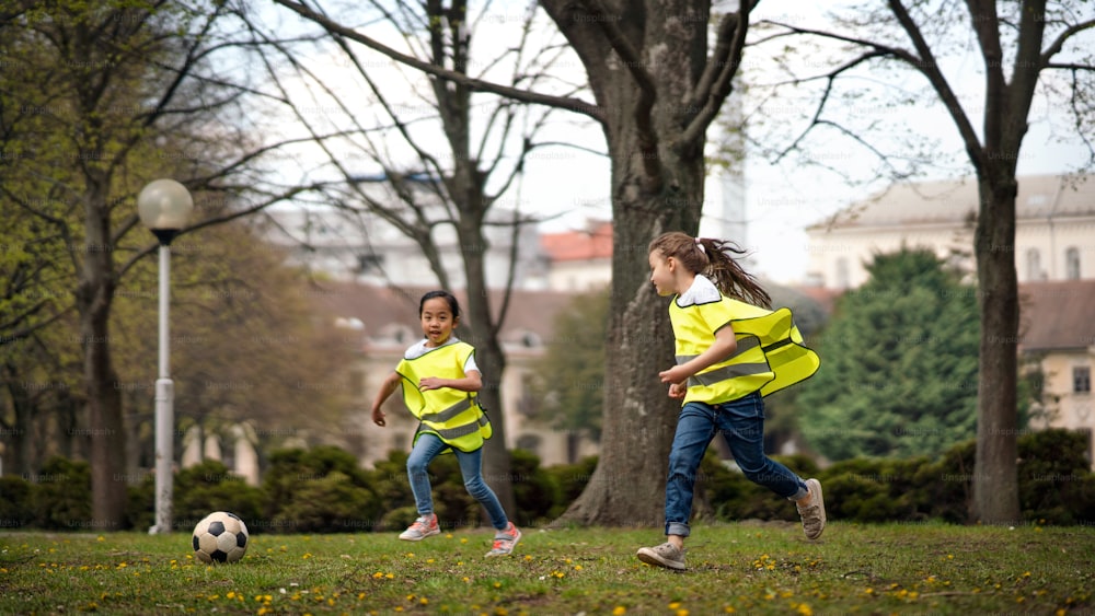 Meninas pequenas felizes jogando futebol ao ar livre no parque da cidade, aprendendo o conceito de educação em grupo.