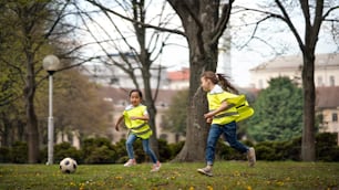 Happy small girls playing football outdoors in city park, learning group education concept.