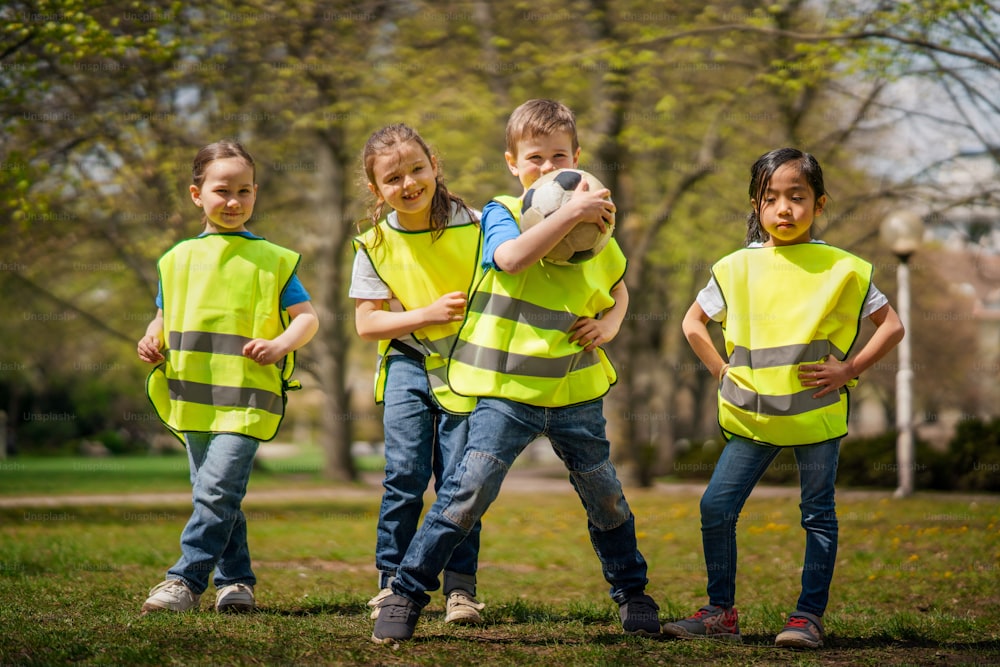 A small children with ball looking at camera outdoors in city park, learning group education concept.