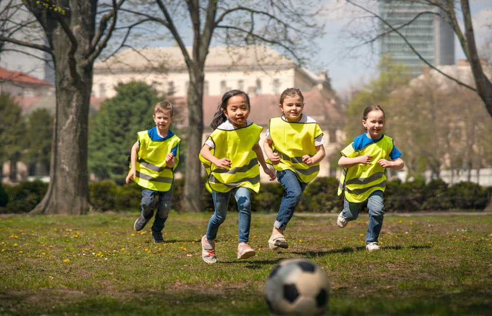Bambini piccoli felici che giocano a calcio all'aperto nel parco cittadino, imparando il concetto di educazione di gruppo.